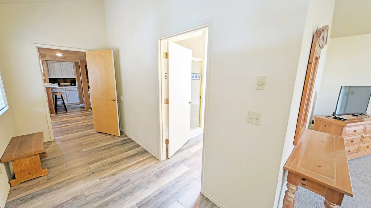 This image features open doors leading to other rooms and a wooden bench positioned near the entryway. The view suggests the point of arrival into the home, emphasizing the first impression guests receive upon entry. The use of natural materials and soft lighting hints at the unique character of the house.