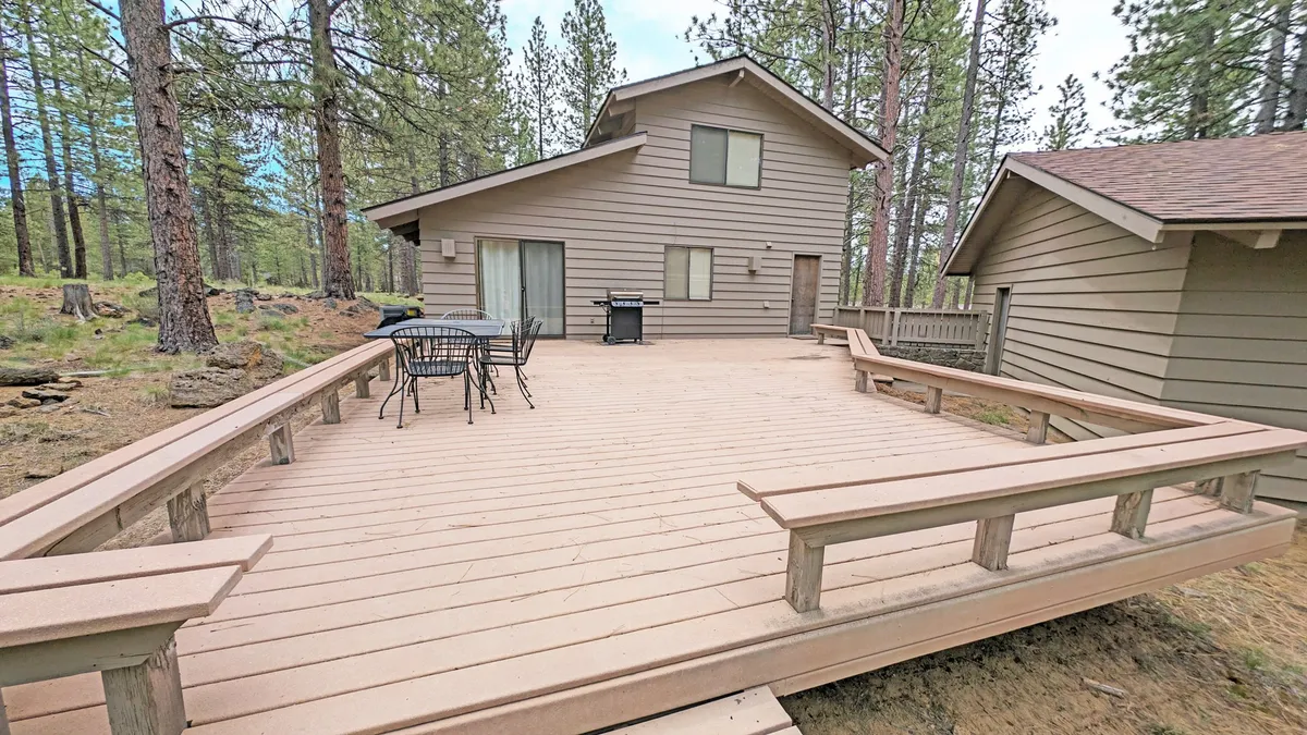 A view of a large deck equipped with outdoor furniture and a grill, surrounded by towering trees. The deck is positioned to catch sunlight and is perfect for social gatherings, outdoor dining, or relaxing after a day of activities. The scene captures the seamless blend of indoor comfort and outdoor adventure.