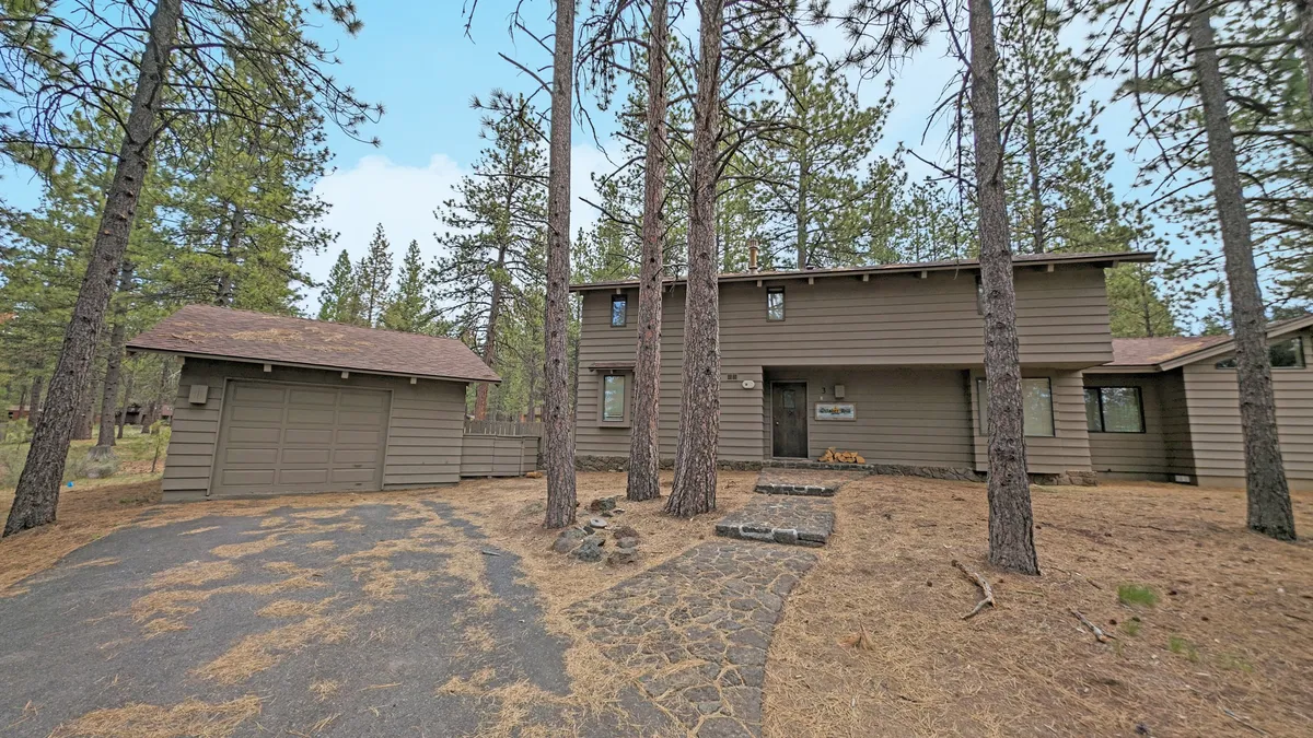 This exterior shot features a spacious two-story home surrounded by tall pine trees, with a stone pathway leading to the entry and an attached garage. The lush setting hints at the tranquility and natural beauty of Sunriver, while the size of the home suggests it’s ideal for groups or families. The open, inviting yard offers space for outdoor activities and relaxation.