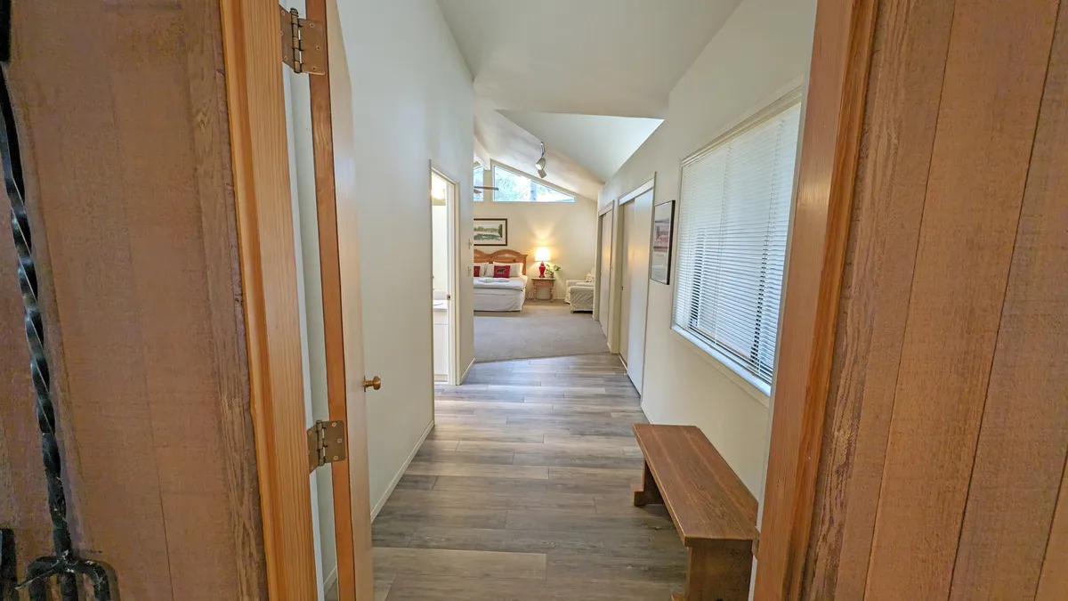 This image displays a wooden bench and doorways leading to different rooms, with soft lighting streaming in from the living area. The scene offers a warm, approachable transition from the entrance into the main living spaces, reinforcing the welcome guests receive after navigating the unique entryway.