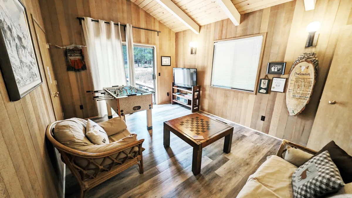 A welcoming interior shot of the Den with a foosball table, checkerboard table, comfortable seating, and large windows bringing in natural light. The scene is set for family game nights, with ample space for everyone to participate and socialize.