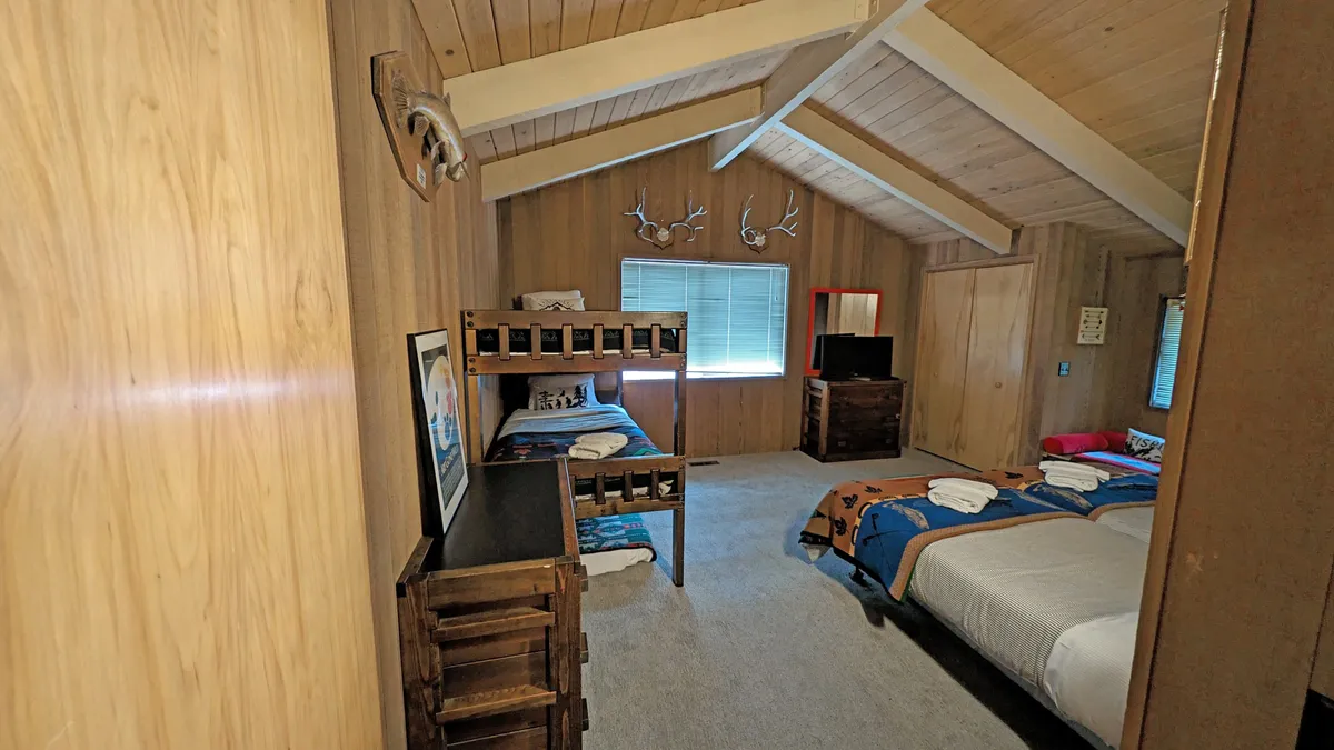 A comfortable family bedroom featuring bunk beds, a double bed, wooden furniture, antler decor, and a large window with views outside. The space feels relaxed and perfect for both kids and adults, supporting flexible sleeping arrangements.